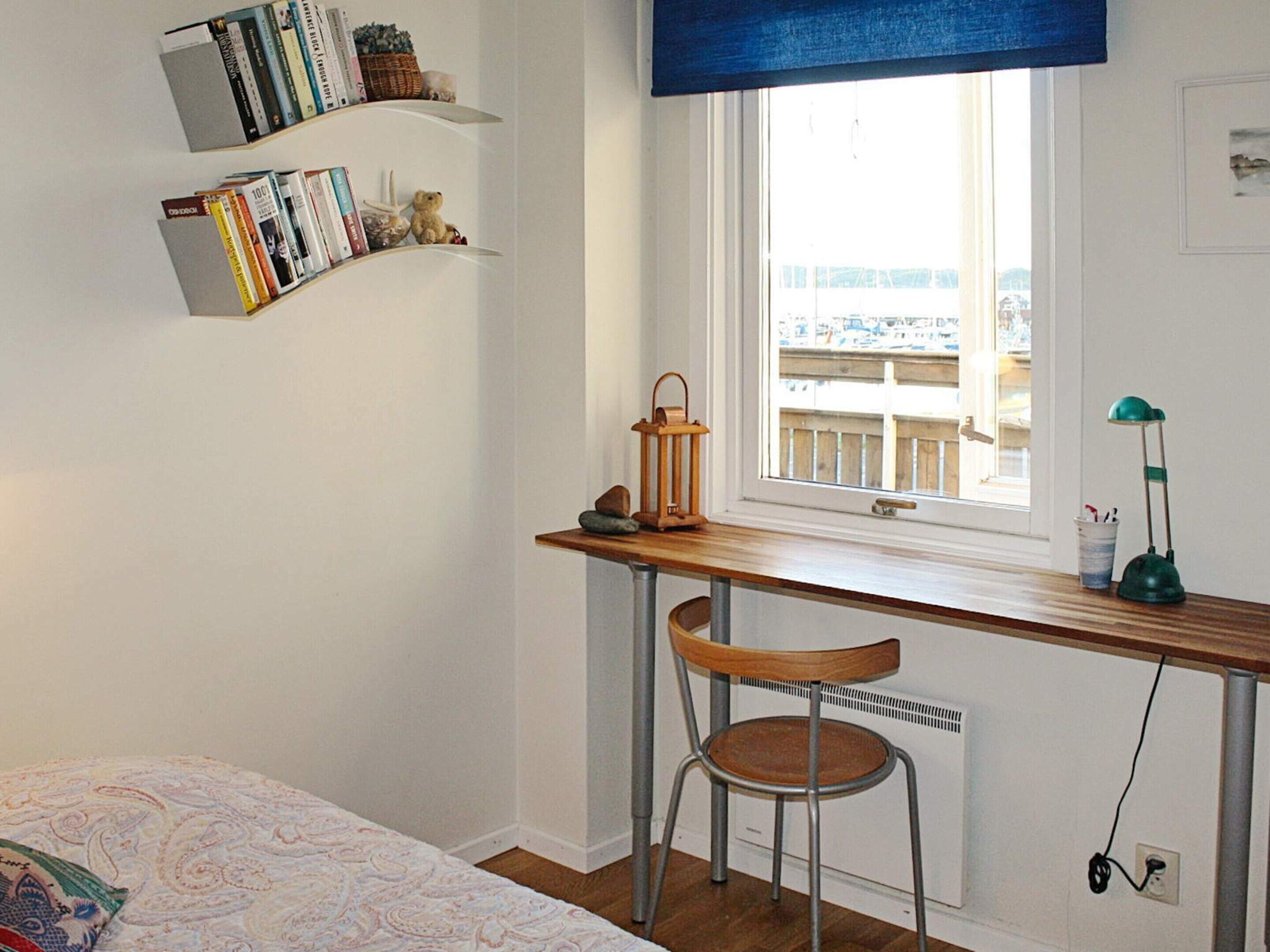 Une chambre à coucher comprenant un lit, un bureau avec une chaise, une fenêtre donnant sur un paysage agréable, ainsi que des étagères remplies de livres et d’objets décoratifs.