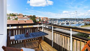 A wooden deck with a table and chairs overlooking a marina with boats and houses in the background. - 4 Person Holiday Home in Ellos (Ellos)