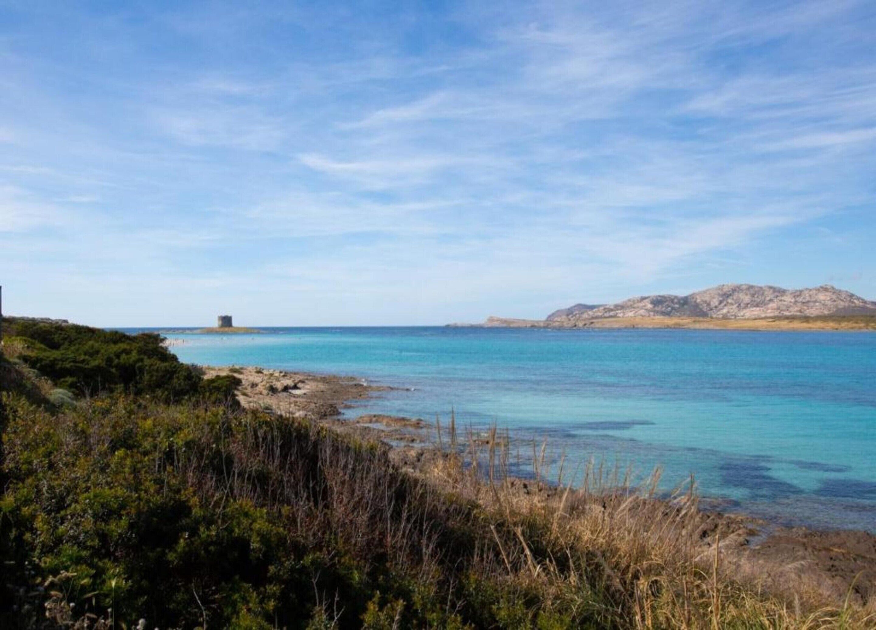 A coastal landscape with clear turquoise waters, rocky terrain, and sparse vegetation.