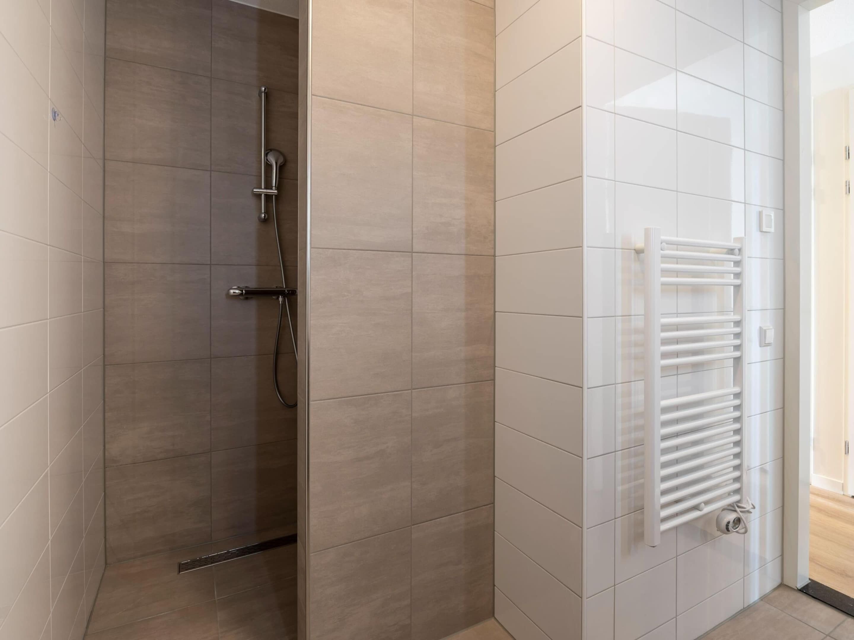 A modern bathroom with a glass-enclosed shower, white tiled walls, and a built-in white towel warmer.
