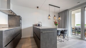 A modern kitchen with a central island, a dining area with a table and chairs, and a view of the outdoors through large windows. - Luxury Apartment in Residence Marina Kamperland - pet Friendly (Kamperland)