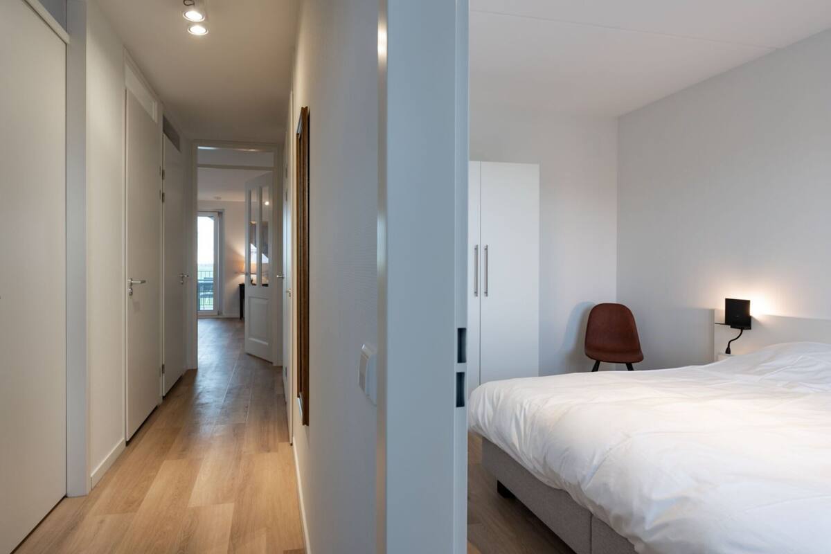 A modern hotel room with a bed, a chair, and a wardrobe.
