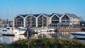 A marina with several boats docked, a modern building with large windows and a flat roof, and a clear blue sky. - Luxury Apartment in Residence Marina Kamperland - pet Friendly (Kamperland)