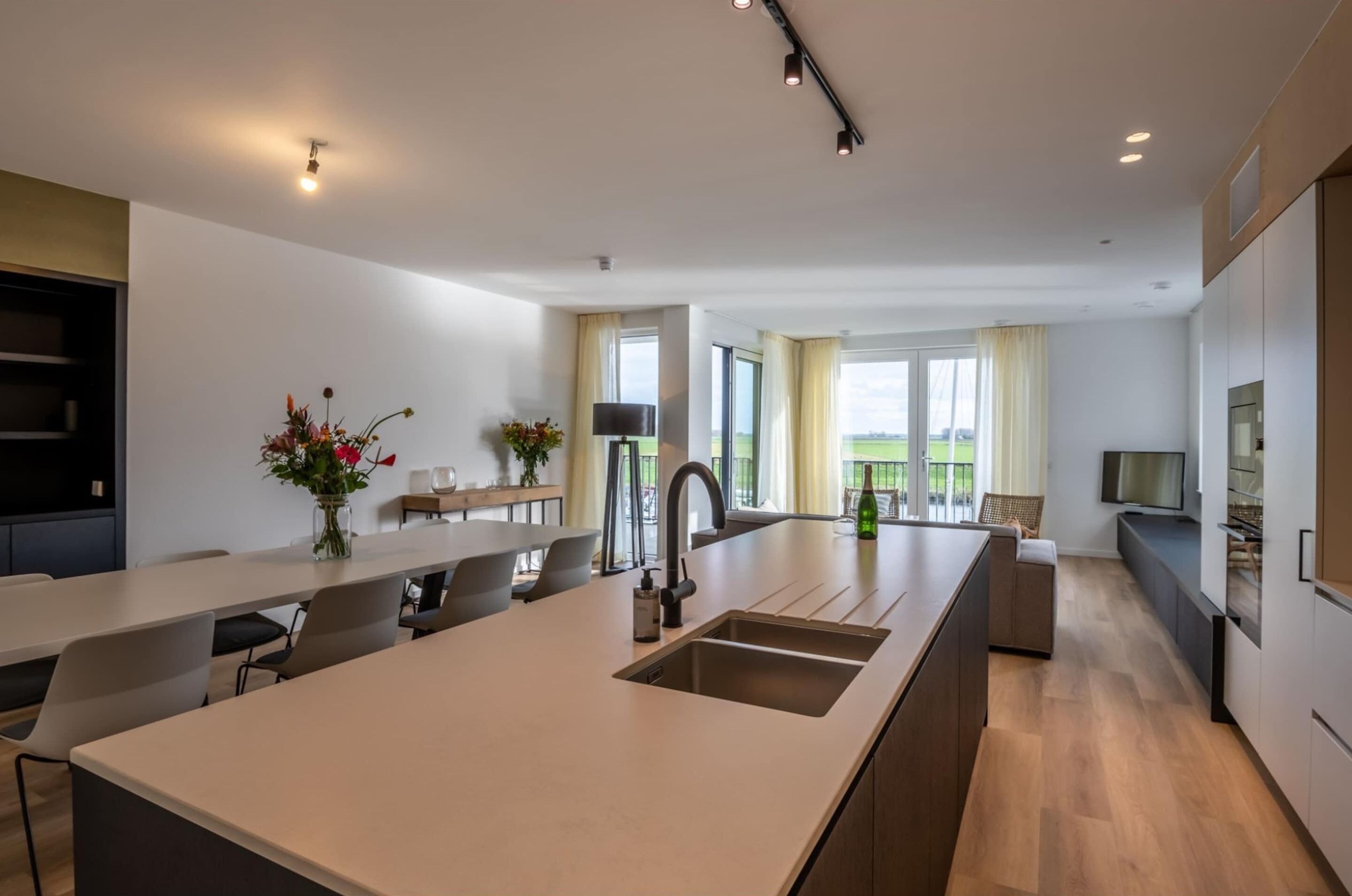 Una cocina moderna con una isla central, una zona de comedor con sillas, un televisor y un balcón con vistas.