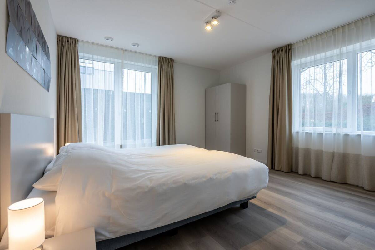 A modern hotel room with a large bed, a wardrobe, and a window with curtains.