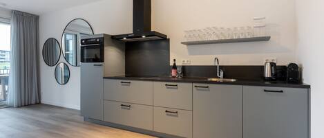 A modern kitchen with grey cabinets, a black range hood, and a built-in oven. There is a wine glass holder on the wall and a coffee maker on the counter.