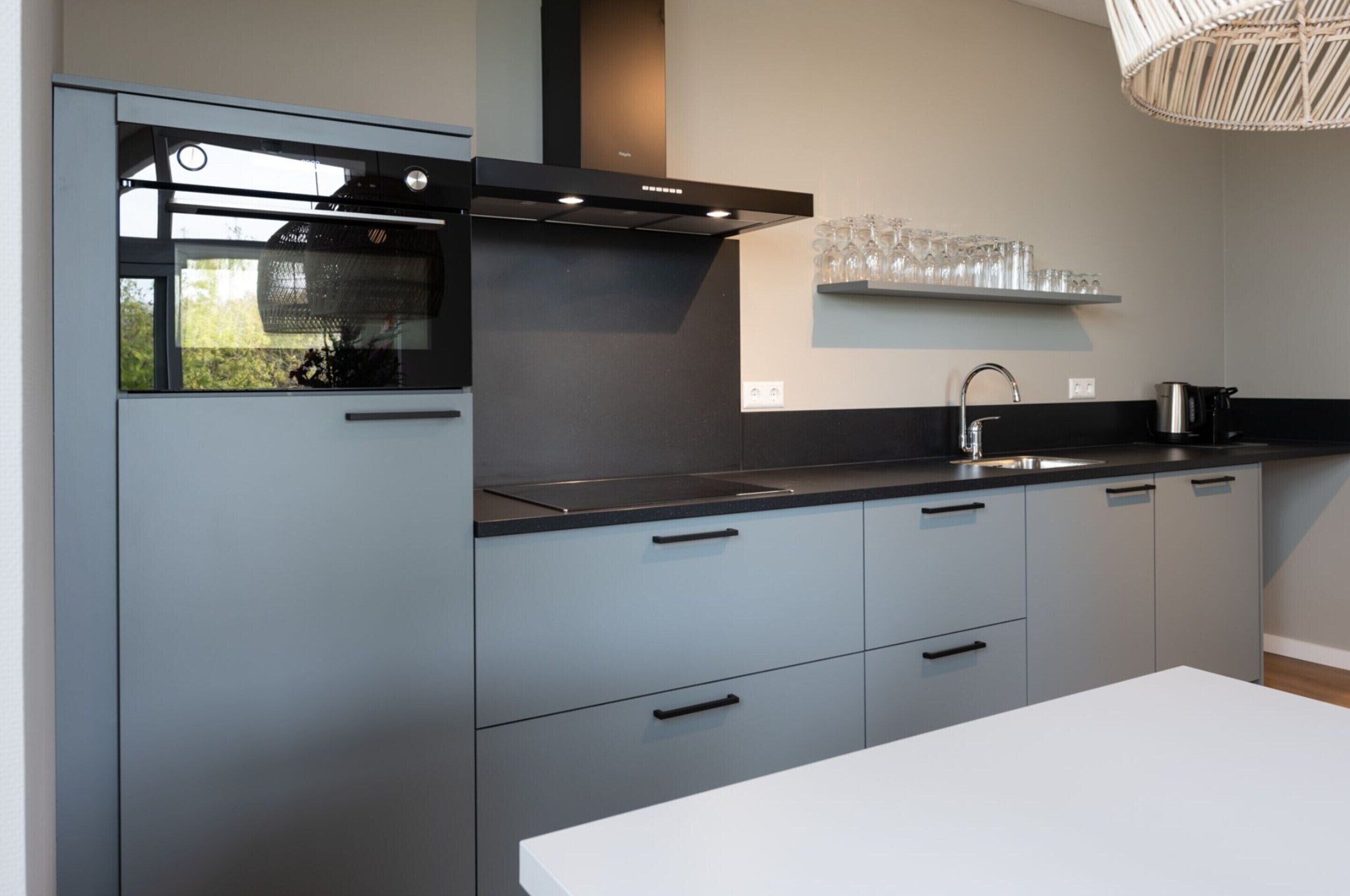 A modern kitchen with grey cabinets, a black countertop, and a stainless steel sink.