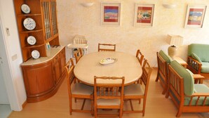 A dining area with a round table surrounded by wooden chairs, a wooden cabinet with shelves, and a sofa with green cushions. - Horacio Villa is Located Near the Center of Vilamoura (Loulé)