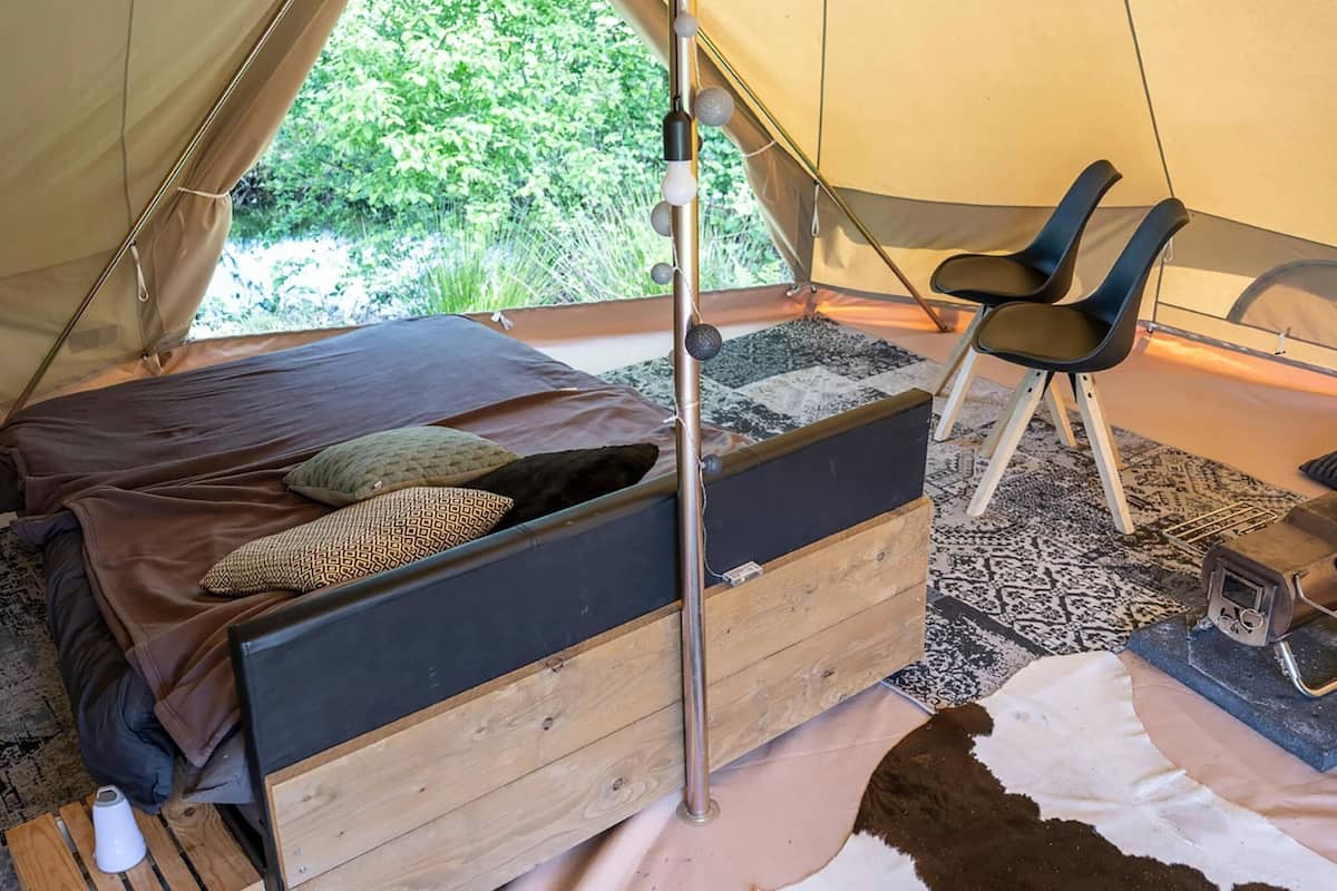 A tent with a bed, two chairs, a heater, and a rug.