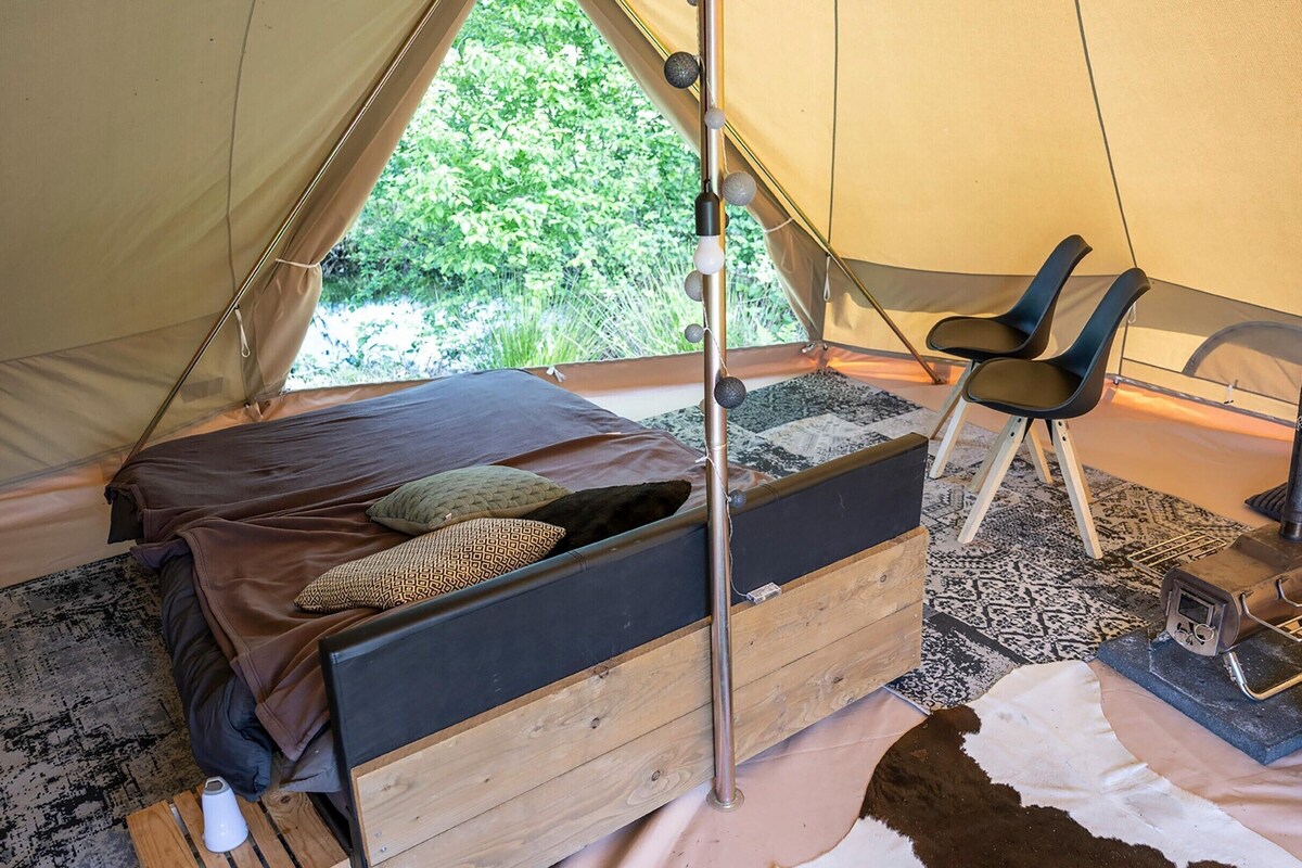 A tent with a bed, a chair, a stove, and a bucket.