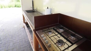 Cocina exterior con estufa a gas, pileta y refrigerador blanco.