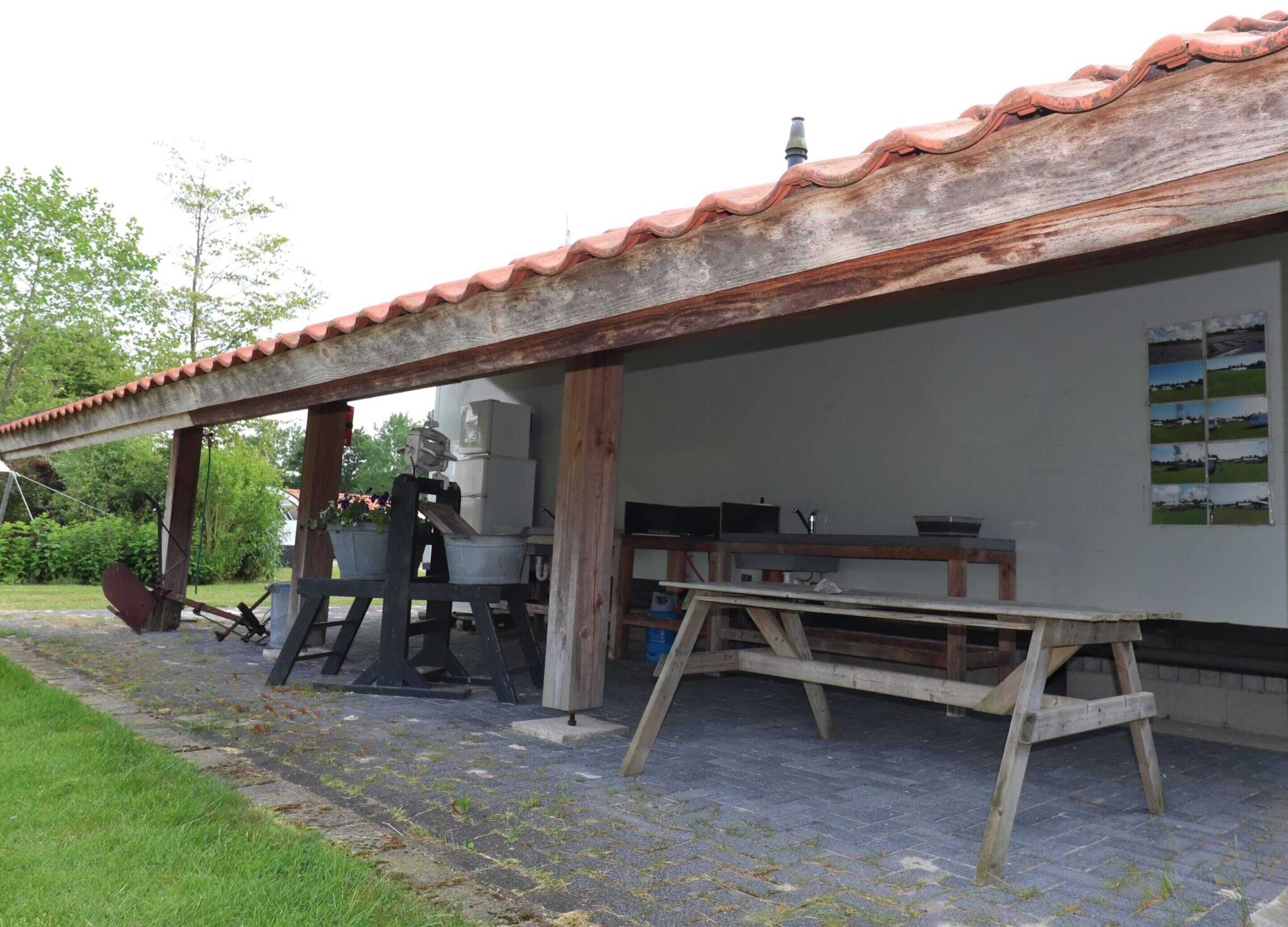 A rustic outdoor kitchen with a tiled roof, a wooden table, and a grill.