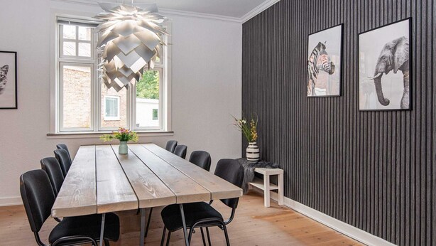 A dining area with a wooden table and black chairs, a hanging light fixture, and framed animal pictures on the wall. - 8 Person Holiday Home in Norre Nebel (Norre Nebel)