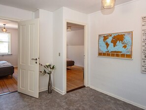 A hallway with a white door, a globe artwork on the wall, and a bed in the adjacent room. - 8 Person Holiday Home in Norre Nebel (Norre Nebel)