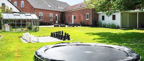 Un jardin avec un trampoline, un jeu d’échecs et une serre.