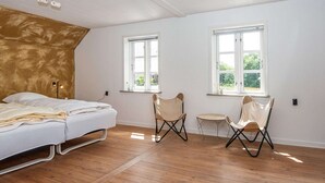 A bedroom with a bed, two chairs, and two windows. - 8 Person Holiday Home in Norre Nebel (Norre Nebel)