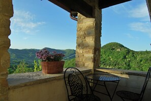 A stone balcony with a view of green hills, a potted plant, and two metal chairs. - Beautiful Apartment in Sestino With Garden (Sestino)