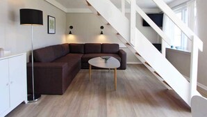 A modern living room with a sectional sofa, a round coffee table, and a staircase with white railings. - 5 Person Holiday Home on a Holiday Park in Gudhjem (Gudhjem)
