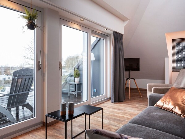 A modern living room with a grey sofa, a black coffee table, and a large window with a view of a balcony and outside buildings. - Apartment Located Directly on the Sneekermeer (Offingawier)