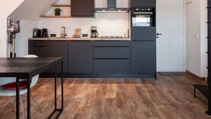 A modern kitchen with dark cabinetry, a built-in oven, and a coffee machine. - Apartment Located Directly on the Sneekermeer (Offingawier)