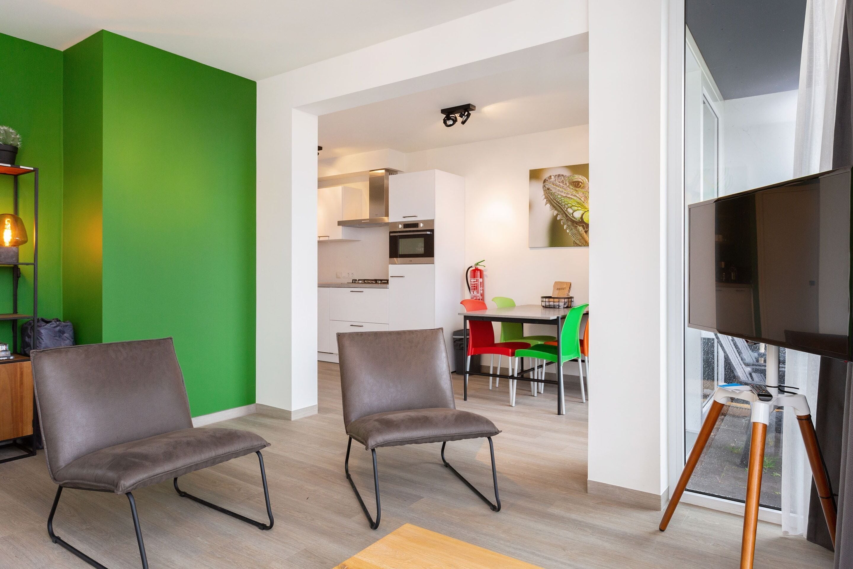 Een moderne woonkamer met twee grijze stoelen, een houten salontafel en een grote flatscreen-televisie op een driepotige standaard.