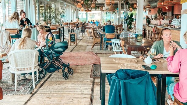 A spacious cafe with high ceilings, hanging wicker lamps, and a variety of seating arrangements including tables and chairs. - Apartment Located Directly on the Sneekermeer (Offingawier)