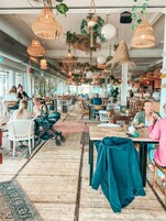 Um café espaçoso com pé direito alto, luminárias de vime suspensas e diversos tipos de assentos, incluindo mesas e cadeiras.