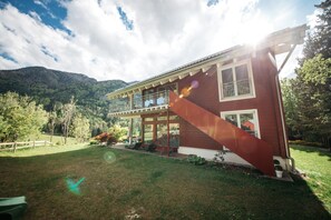 Une maison à deux étages dotée d’un balcon, entourée d’une pelouse bien entretenue et d’arbres.