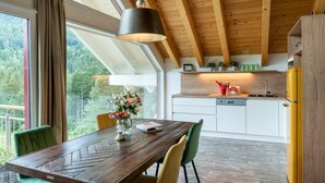 A modern kitchen with wooden beams, a dining table, chairs, and a view of greenery outside. - Lush Apartment in Sankt Michael ob Bleiburg (Feistritz ob Bleiburg)
