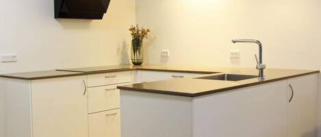 A modern kitchen with white cabinetry, a central island, a built-in oven, and a pendant light.
