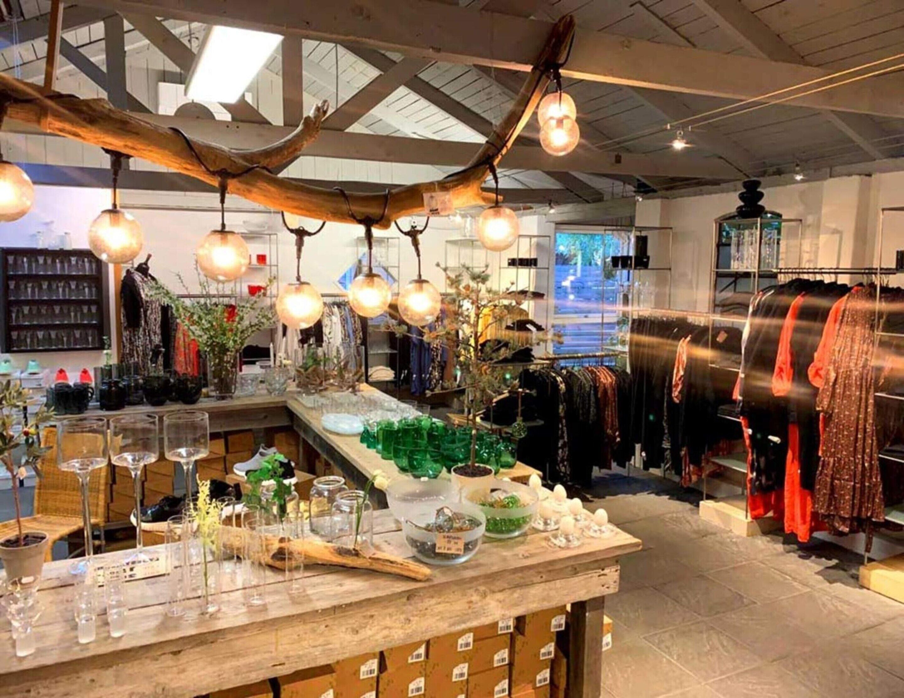 A boutique hotel interior with a wooden bar area, clothing racks, and hanging lights.