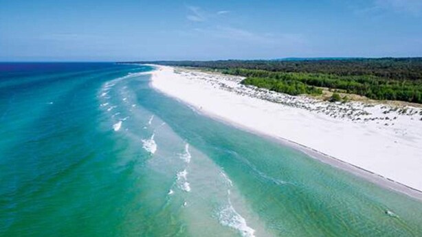 Vue aérienne d’une plage aux eaux turquoise et au sable blanc.