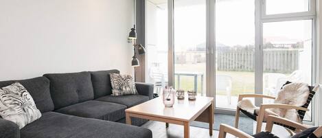 Una sala moderna con un sofá gris, una mesa de centro de madera y un sillón con cojín negro y blanco.