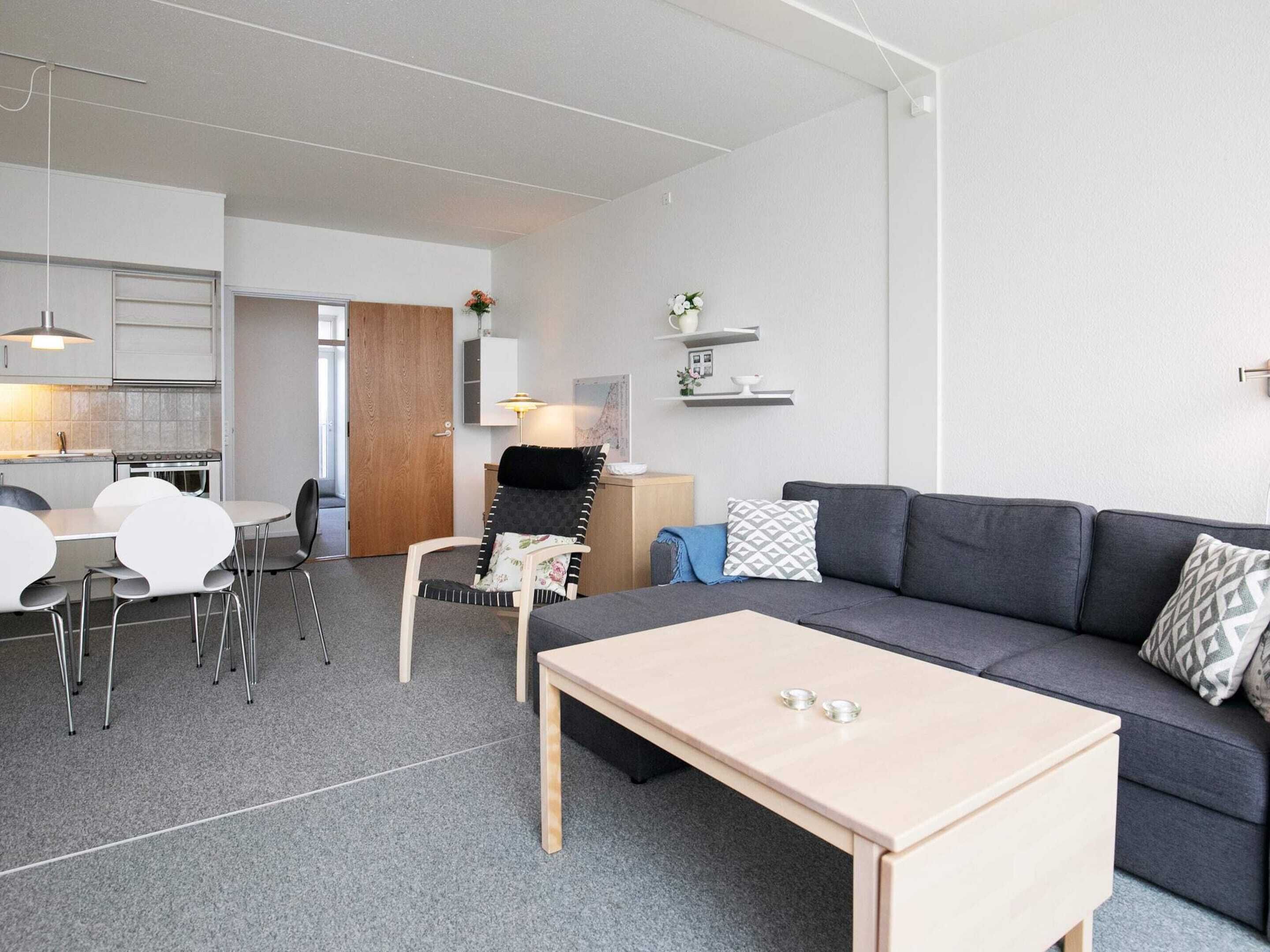 A modern living room with a grey sofa, a wooden coffee table, and a dining area with a white table and chairs.