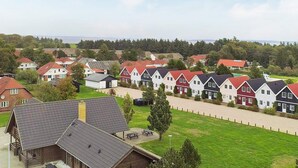 Une rangée de maisons traditionnelles aux toits rouges, un chalet en bois et une zone herbeuse avec des tables de pique-nique.