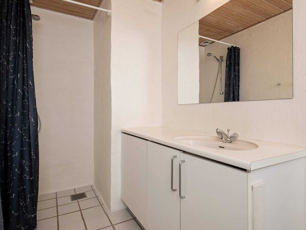 Un baño con lavamanos blanco, un espejo y una ducha.