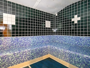 A small, tiled pool area with a blue mosaic border and a white cross on the wall.