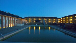 Une piscine avec une fontaine au centre, entourée d’un bâtiment doté de nombreux balcons et d’une clôture.