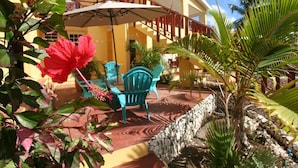 Un patio con un edificio amarillo, mobiliario exterior y plantas tropicales.