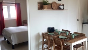 Una habitación compacta con cama, una mesa de comedor con sillas, una pequeña cocina y un reloj en la pared.