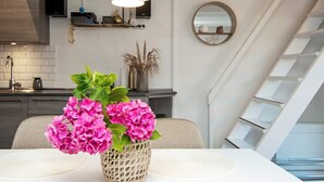 Una cocina moderna con una lámpara de techo blanca, una mesa de comedor con una cesta de flores rosas y una escalera con barandilla blanca.