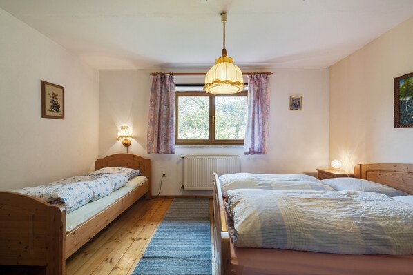 A room with two wooden beds, a window with curtains, a radiator, and a hanging light fixture.