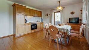 A compact kitchen with wooden cabinets and a dining area with a table and chairs. - Farmhouse in Neukirchen Near Heiligen Blut (Neukirchen Beim Heiligen Blut)