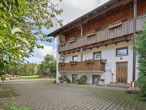 Un bâtiment à deux étages doté de balcons en bois, de plantes en pot et d’une cour dallée.