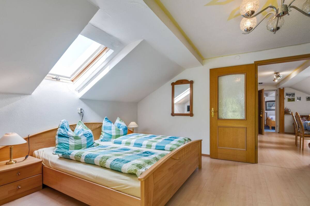 Een slaapkamer met een schuine plafond, dakraam, houten bed, nachtkastje, spiegel en een deur naar een andere kamer.