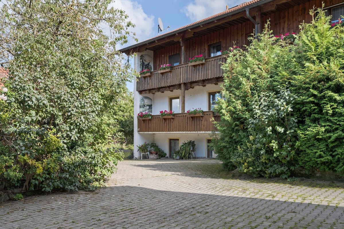 Een klassiek chalet met houten balkons, een geplaveid binnenterrein en weelderige begroeiing.