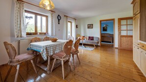 A dining area with a wooden table and chairs, a hanging light fixture, and a view into another room with a bed and a blue wall. - Farmhouse in Neukirchen Near Heiligen Blut (Neukirchen Beim Heiligen Blut)
