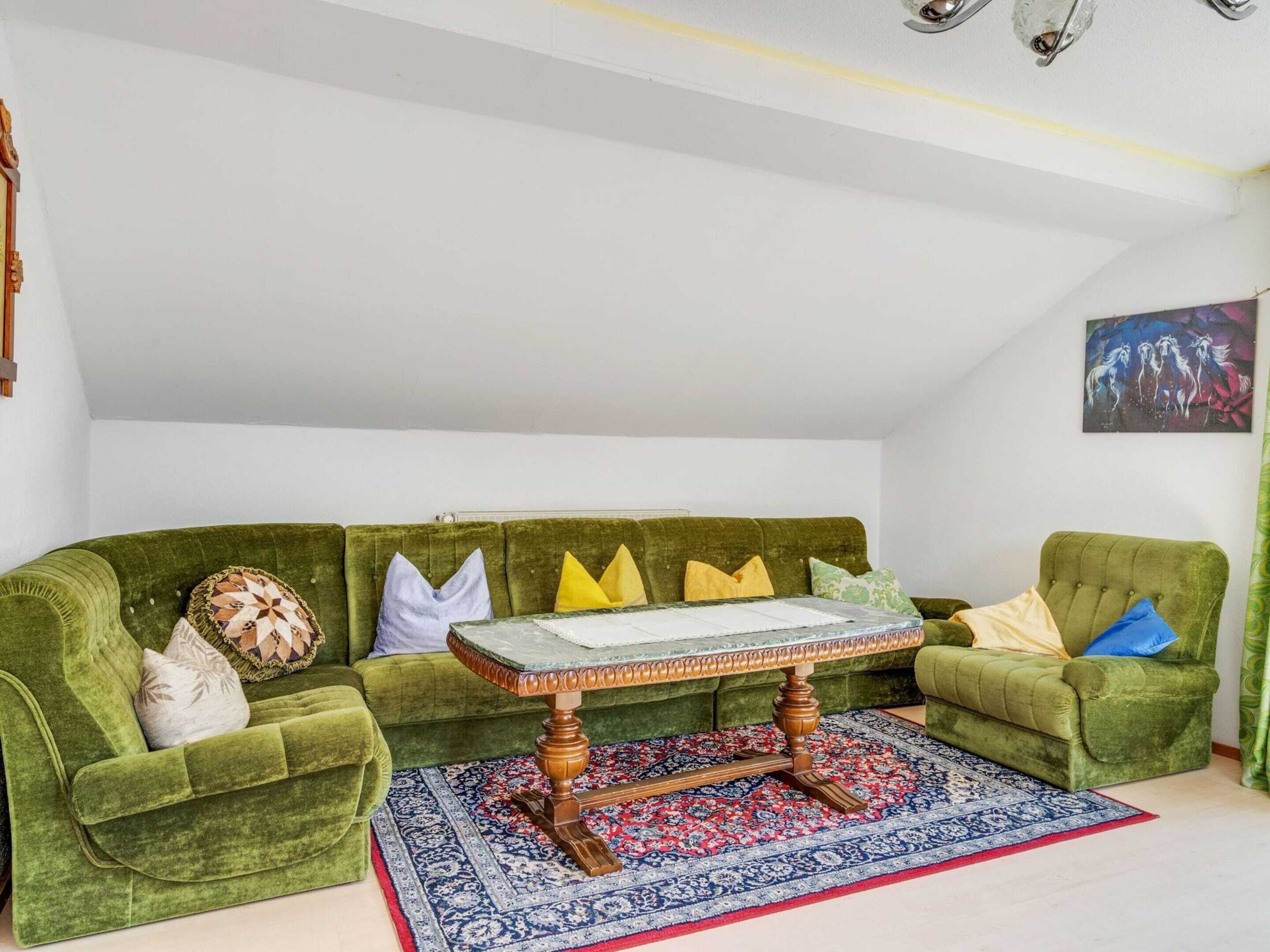 Un divano in velluto verde con un tavolino in legno e un tappeto decorato in una stanza dalle pareti bianche e con una luce a soffitto.