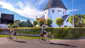 Två cyklister på en asfalterad stig med ett historiskt torn och en vit byggnad i bakgrunden.