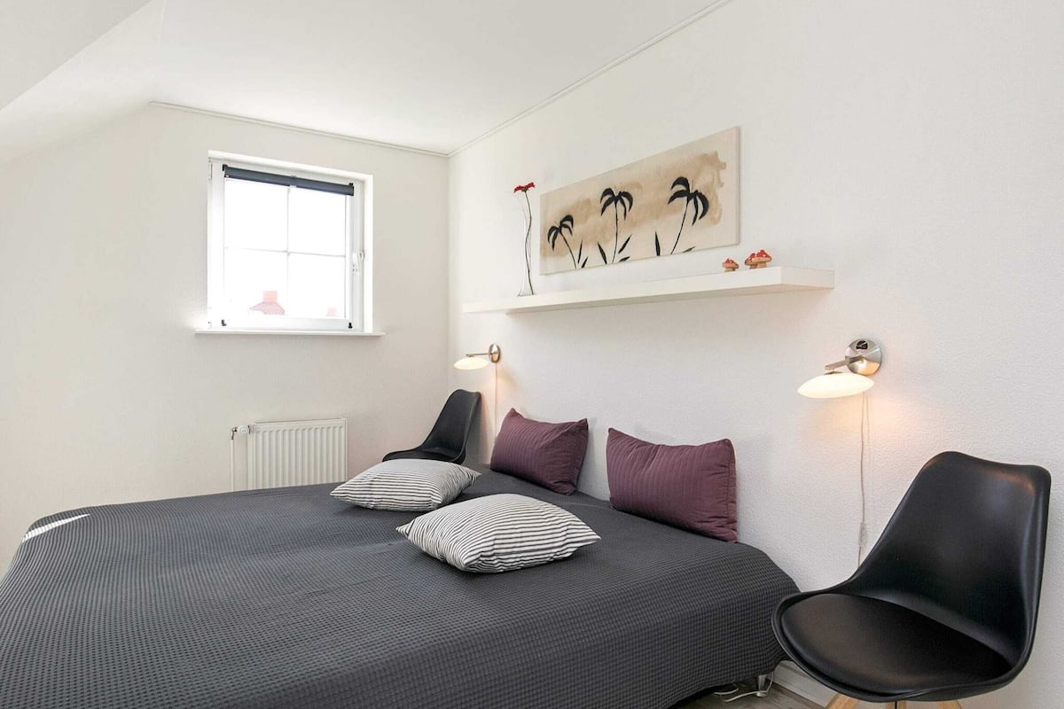 A bedroom with a bed, two bedside lamps, a window, and a wall-mounted shelf with decorative items.